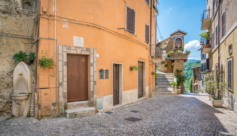 Strada acciottolata in un villaggio italiano con edifici arancioni e beige, scale che portano in salita.