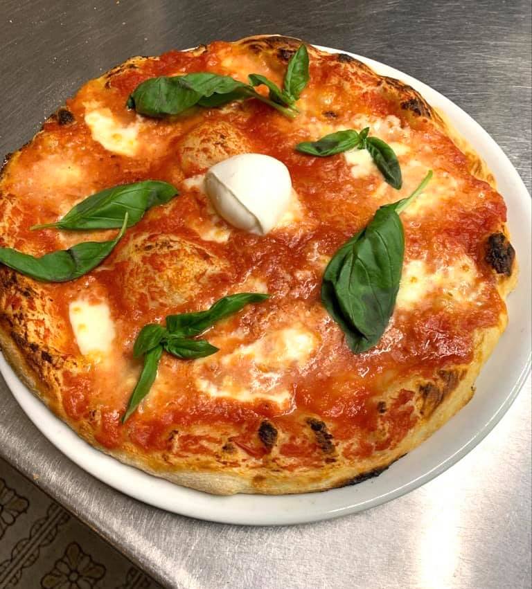 Pizza condita con salsa di pomodoro, mozzarella e basilico, servita su un piatto bianco.