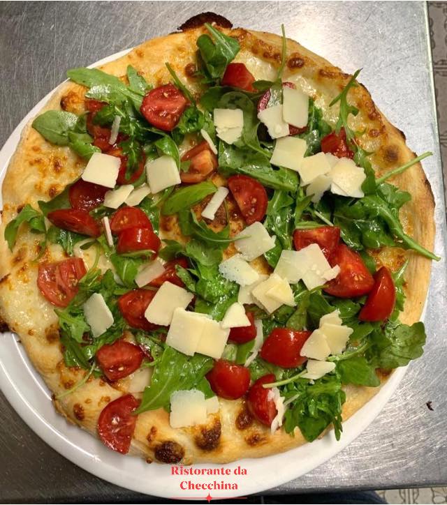 Pizza con rucola, pomodorini e formaggio a scaglie, servita su un piatto bianco.