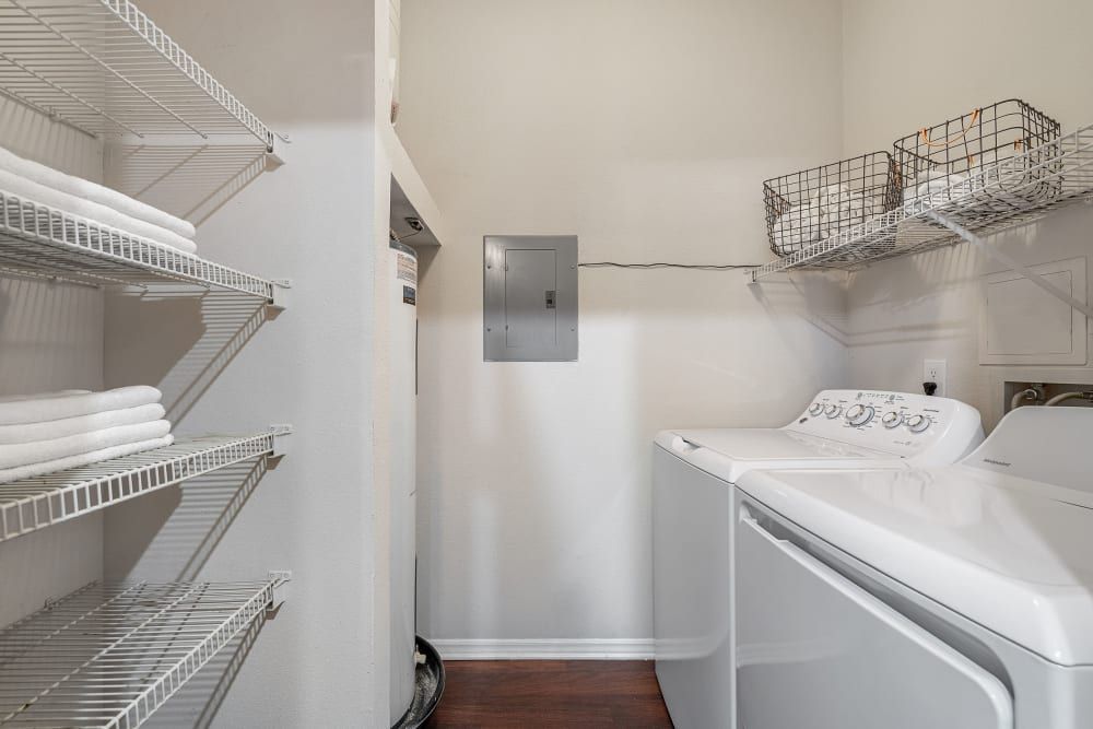 a laundry room with a washer and dryer and wire shelves at Marquis Carmel Valley in Charlotte, NC.