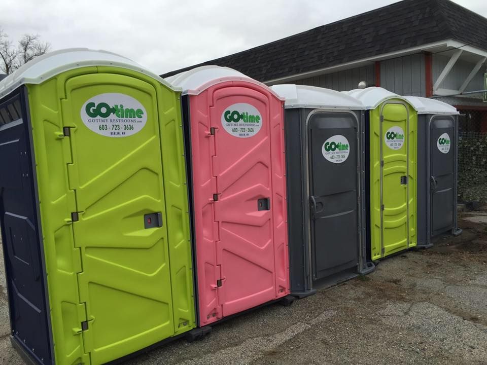 Row of colorful portable toilets in front of a building; green, pink, gray, and blue.