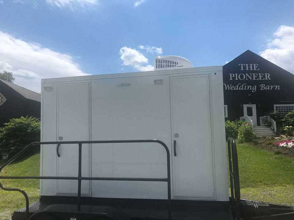 White portable restroom trailer parked in front of a barn with