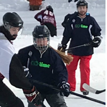 People playing ice hockey outdoors in winter. Player in center wearing a 