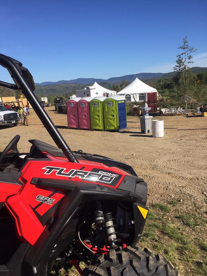 Red ATV, portable toilets, white tents, and mountains under a blue sky.