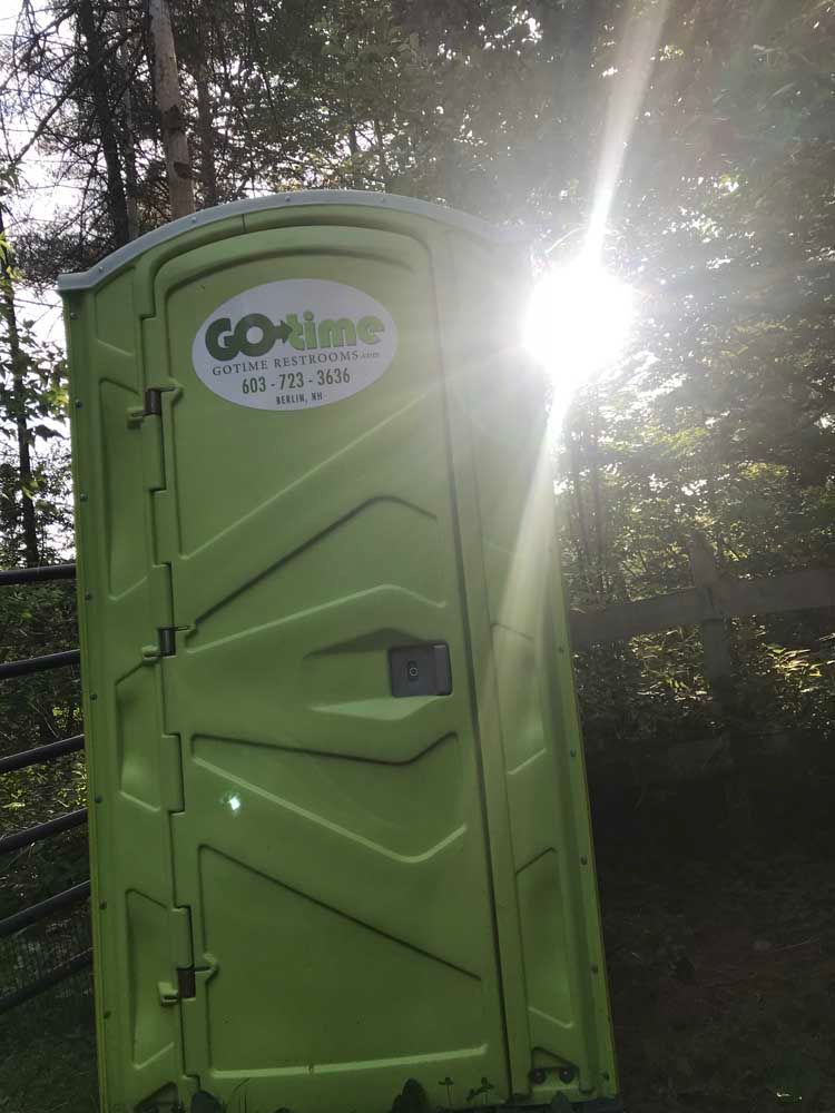 Green portable toilet outdoors with sunlight shining.