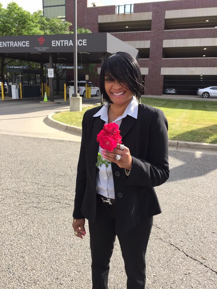 Woman in suit holding red roses in front of hospital entrance.