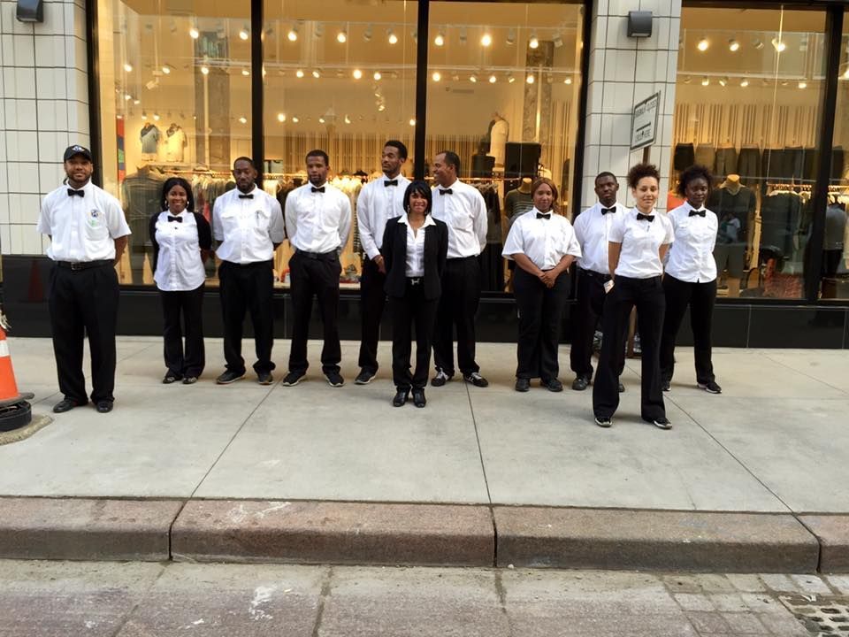 A group of people in formal attire outside a store. They are wearing white shirts and black pants.