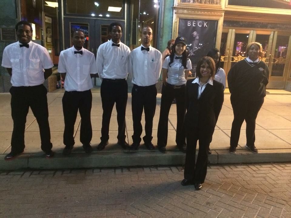 Group of service workers posing in front of a building with “Beck” sign. They are dressed in black and white.