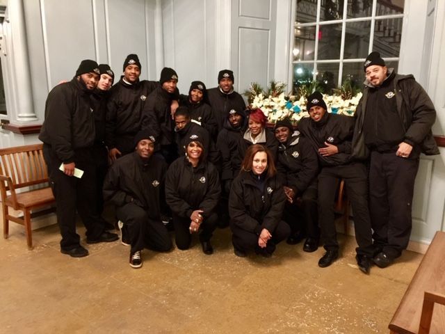 Group of people, all in black, posing near a floral arrangement inside a building.