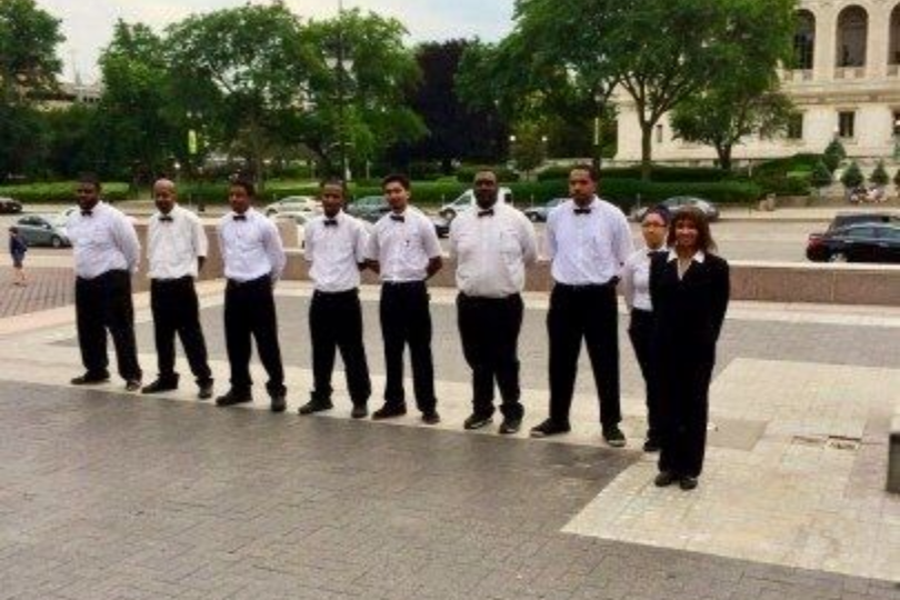 A group of people in formal attire stand outdoors in front of a building.