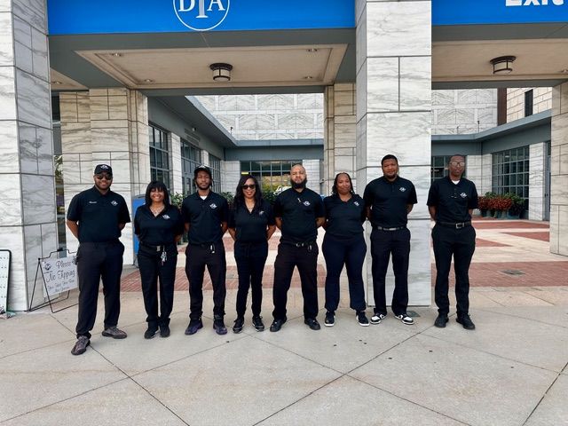 Group of eight people in black uniforms standing in front of a building with