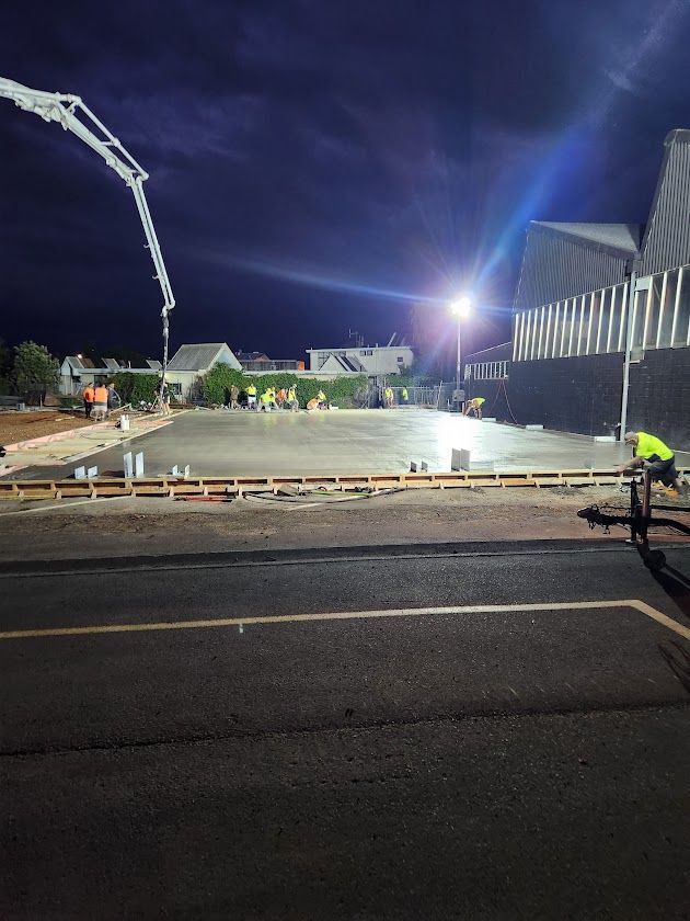 A construction site at night with a concrete pump in the background.
