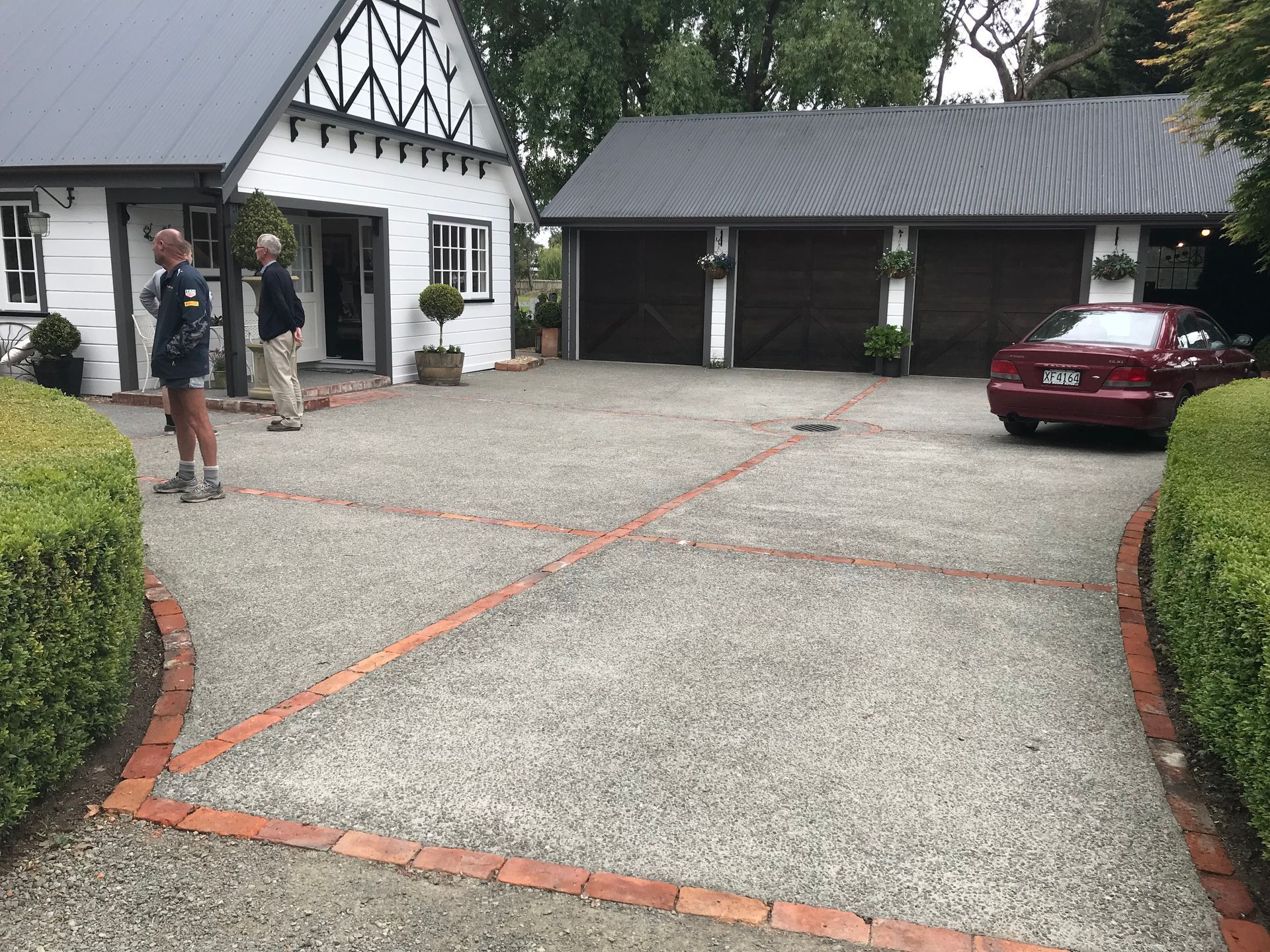 Two men are standing in front of a house with a car parked in the driveway.