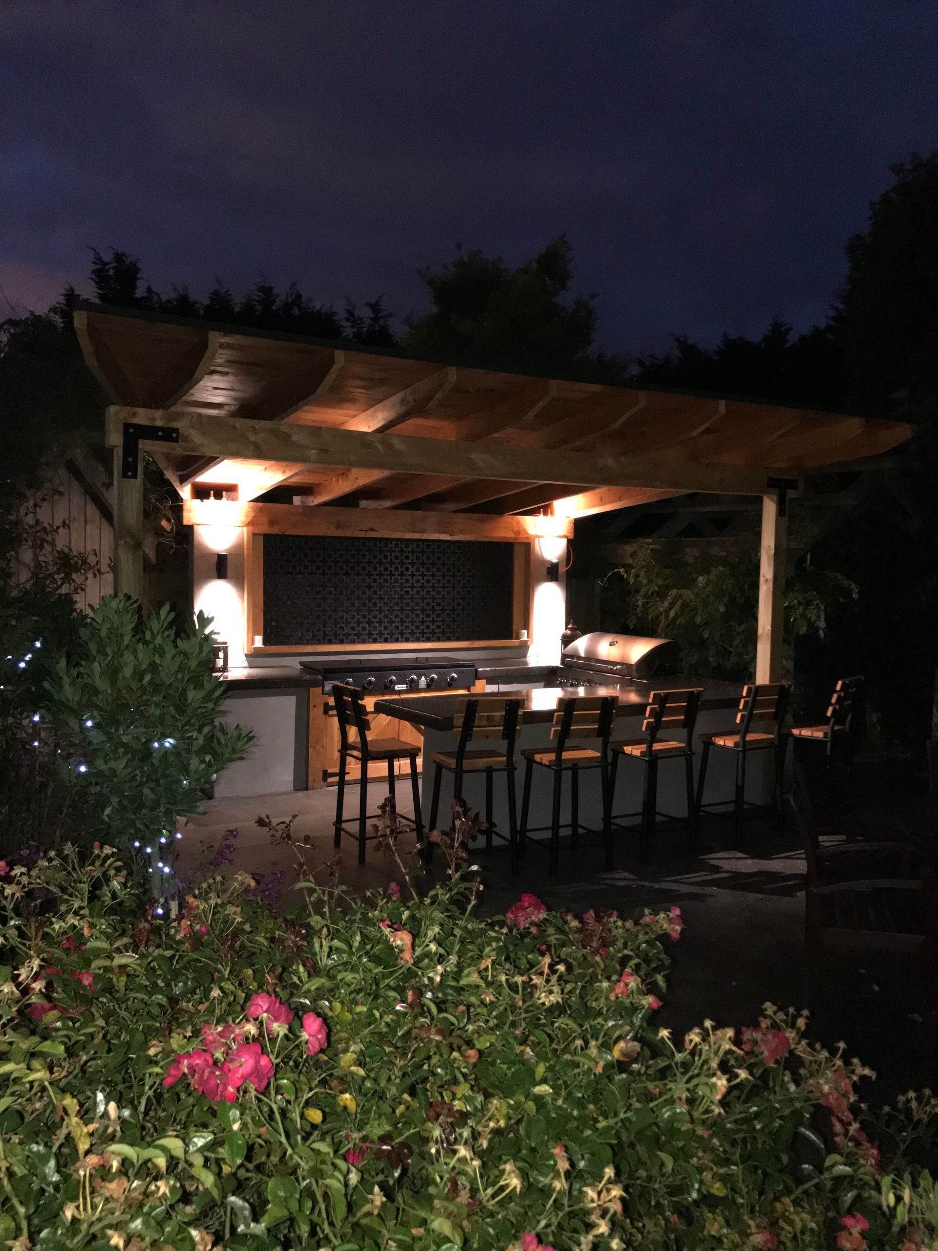 A patio with a table and chairs under a pergola at night