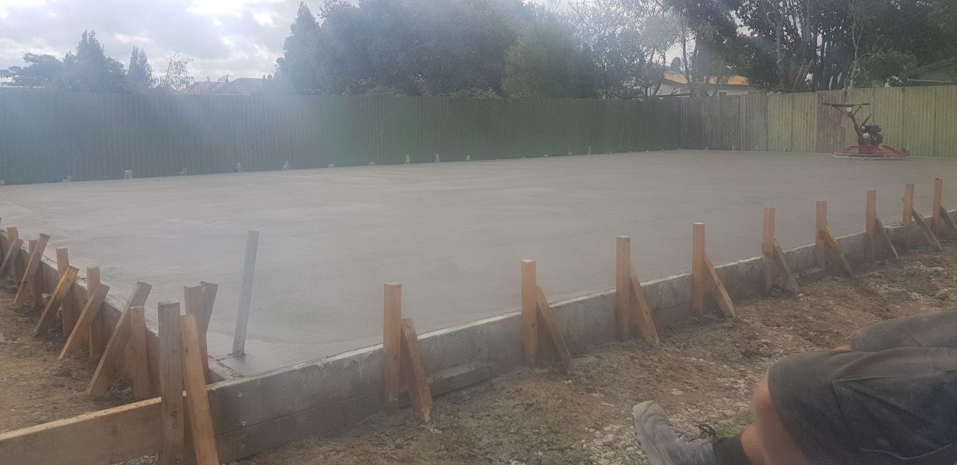 A man is laying concrete on the ground in a backyard.