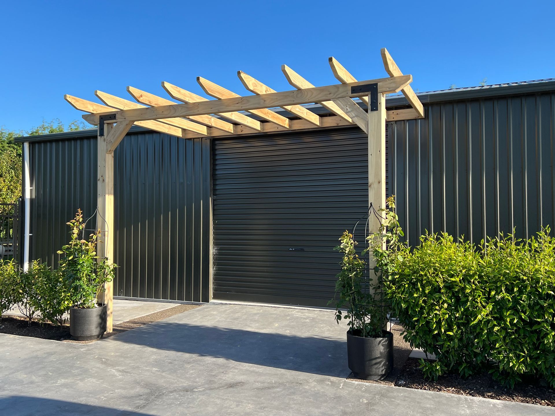 A wooden pergola is sitting in front of a black building.