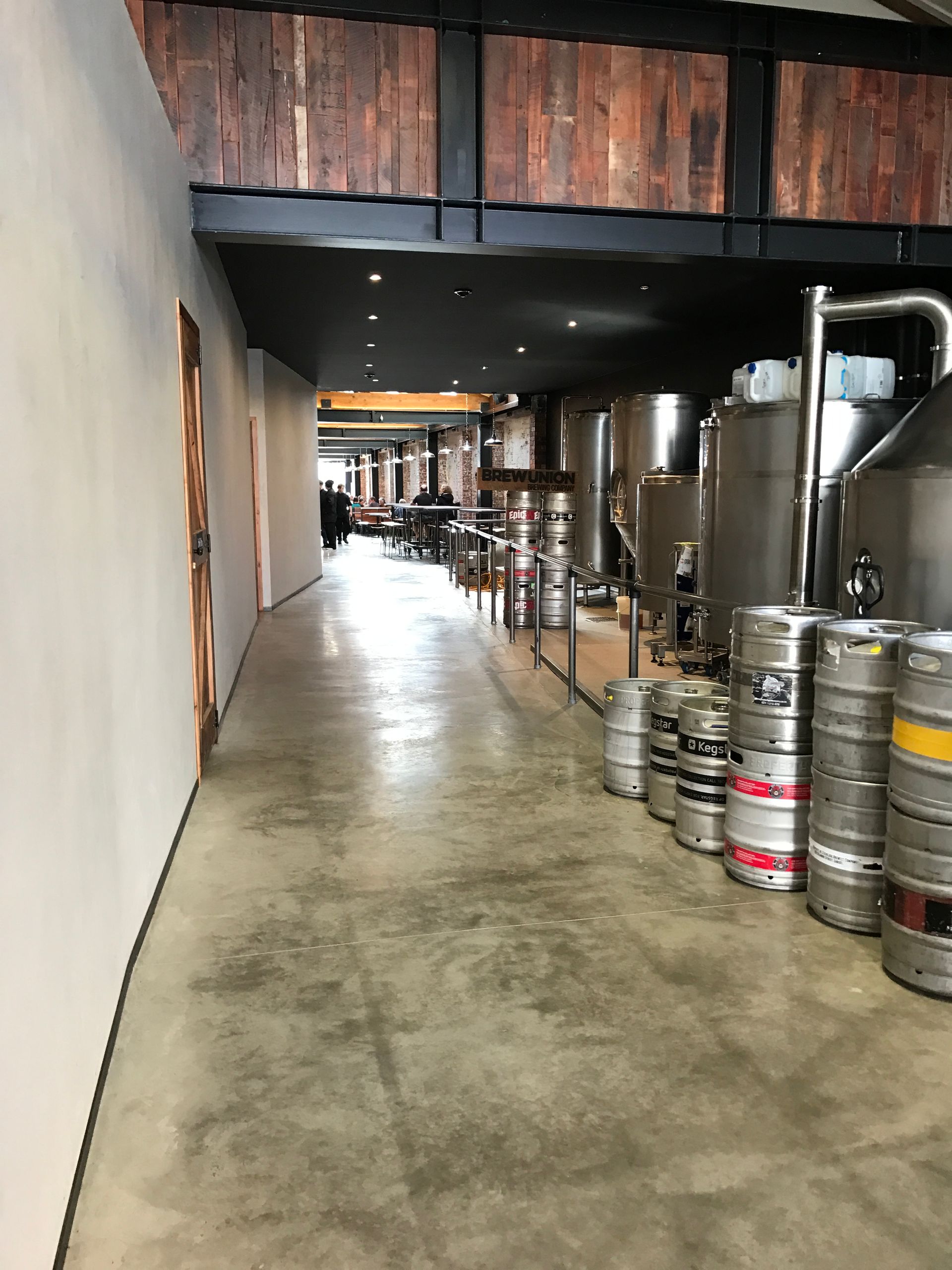A long hallway filled with barrels and tanks in a brewery.