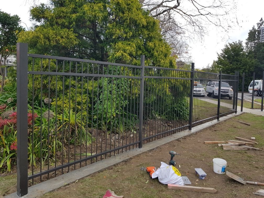 A black metal fence is being built in a yard.