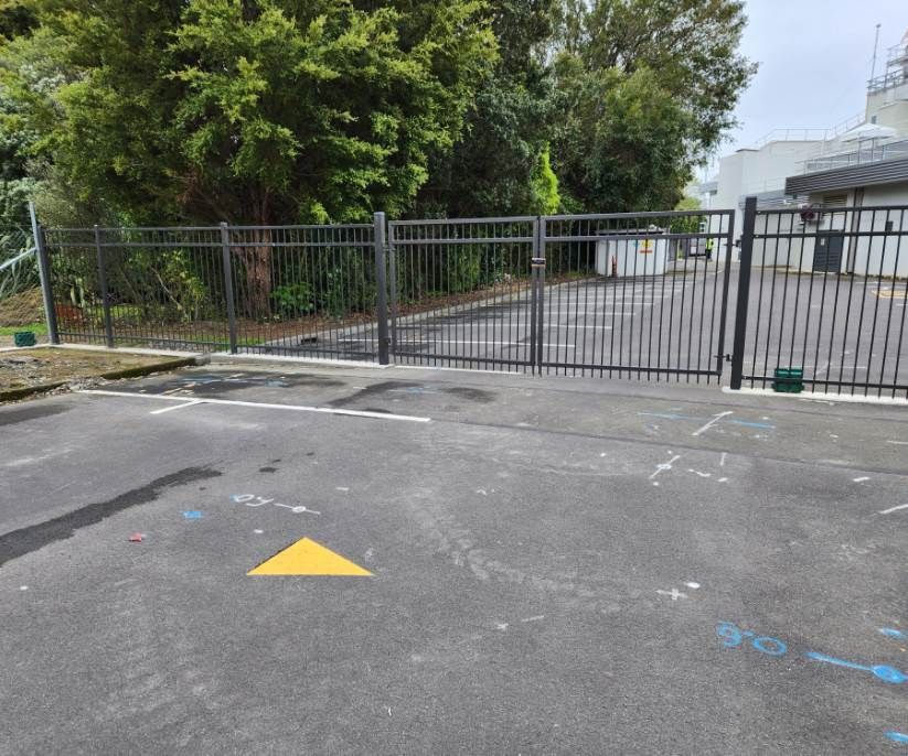 A parking lot with a fence and a yellow arrow on the ground.