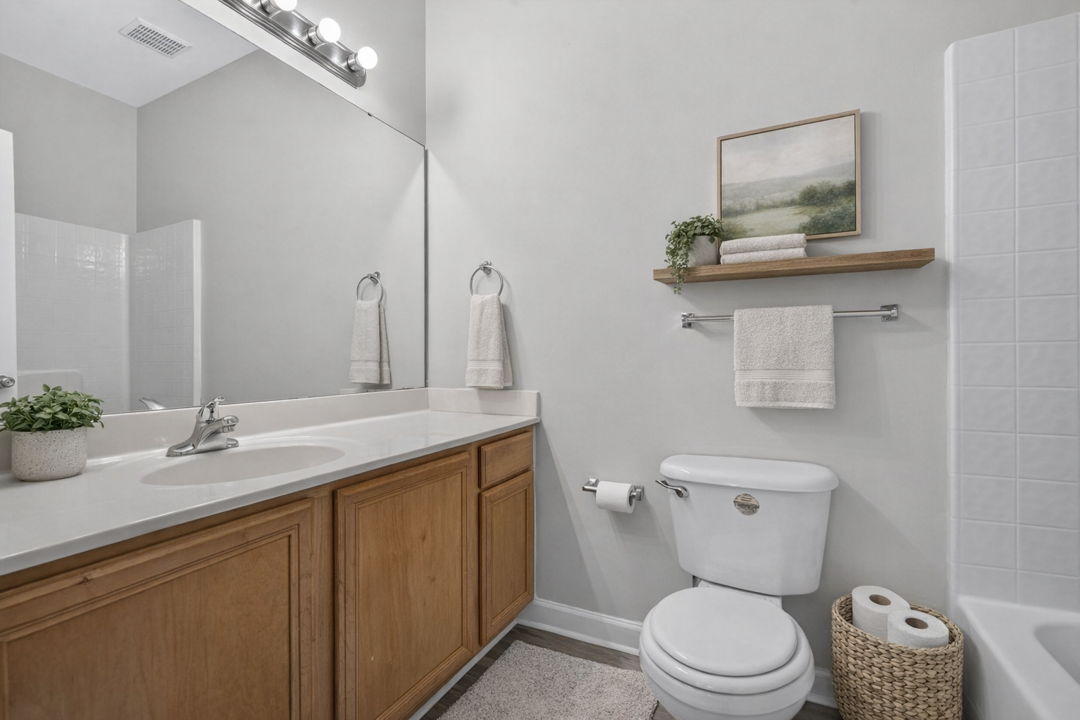 A light gray bathroom featuring a wood vanity with a white countertop, a toilet, a bathtub, and wall-mounted decor.