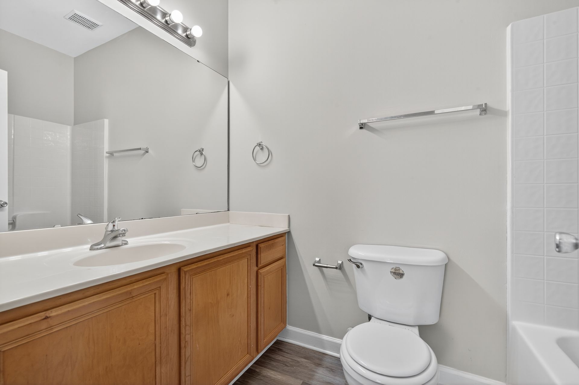 A bathroom with light gray walls, wooden vanity cabinets, a large mirror, a white toilet, and a bathtub.