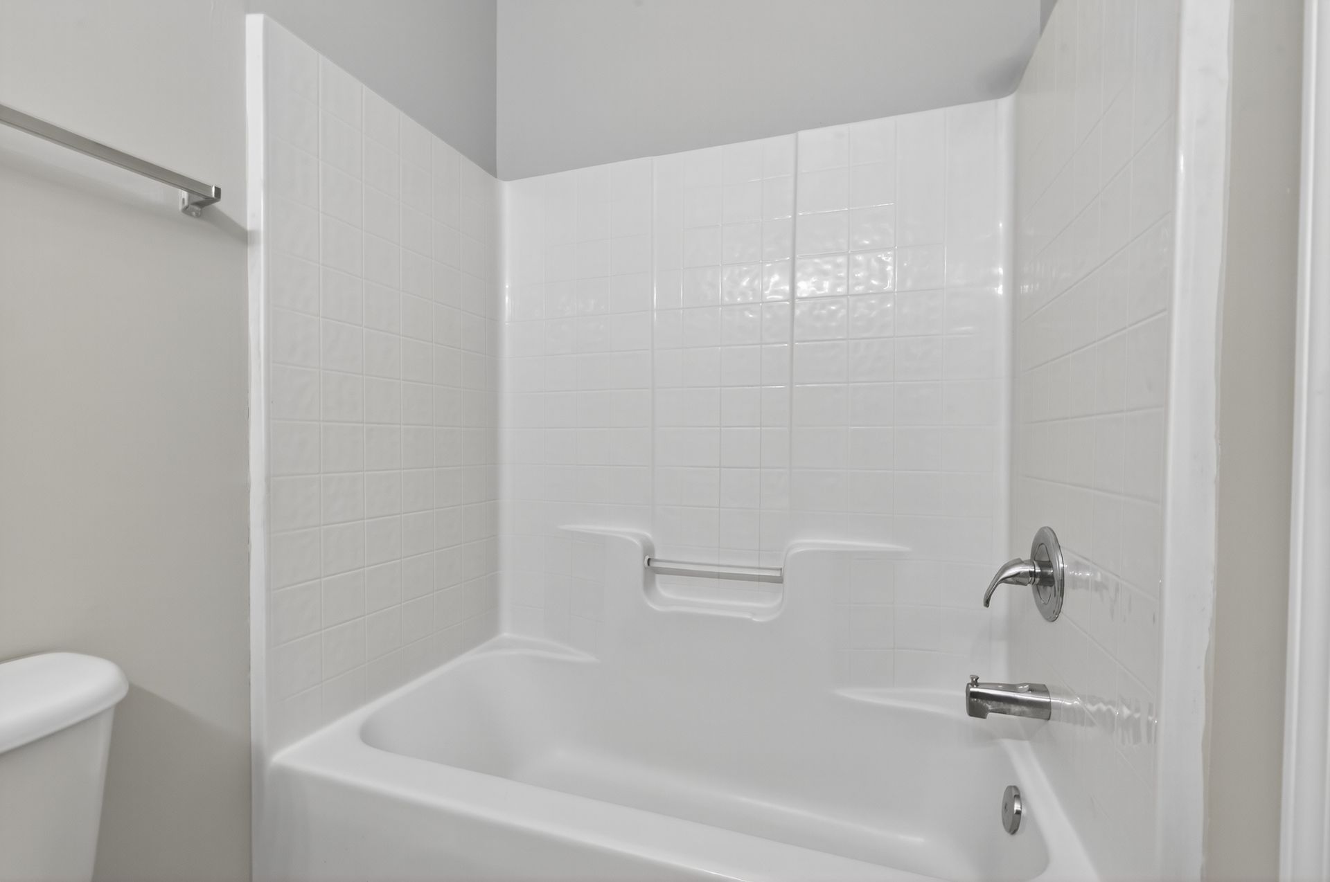 A white bathtub and shower surround with a metal faucet and built-in shelving in a bathroom with light gray walls.
