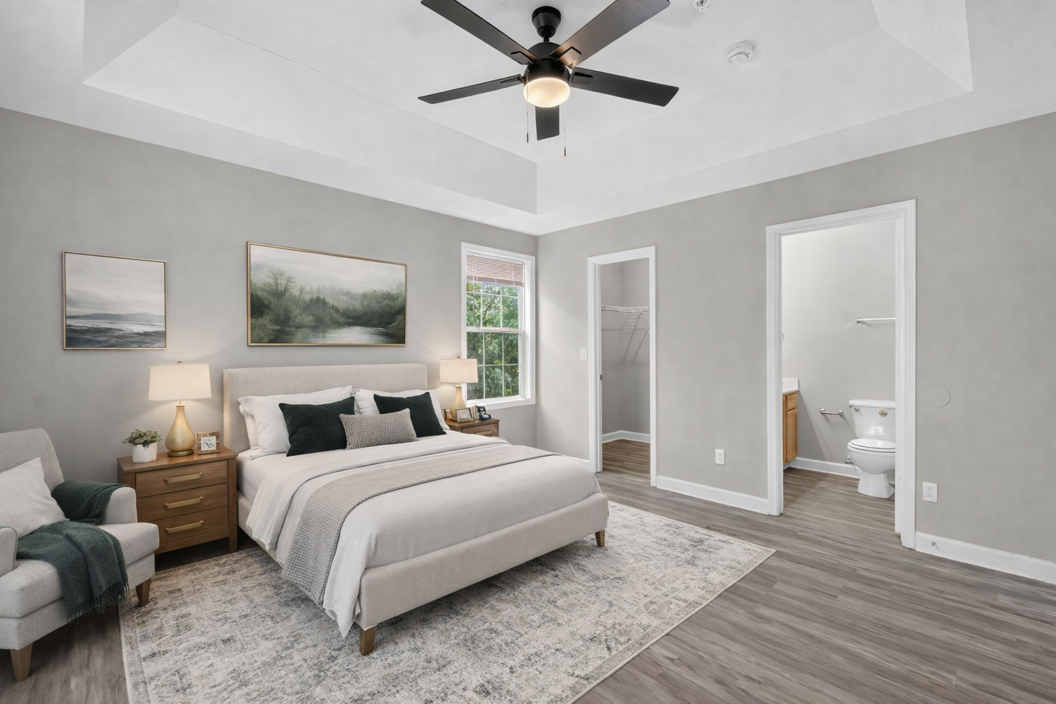 A modern, neutral-toned bedroom with a queen bed, a gray armchair, and two doorways leading to a walk-in closet and bathroom.