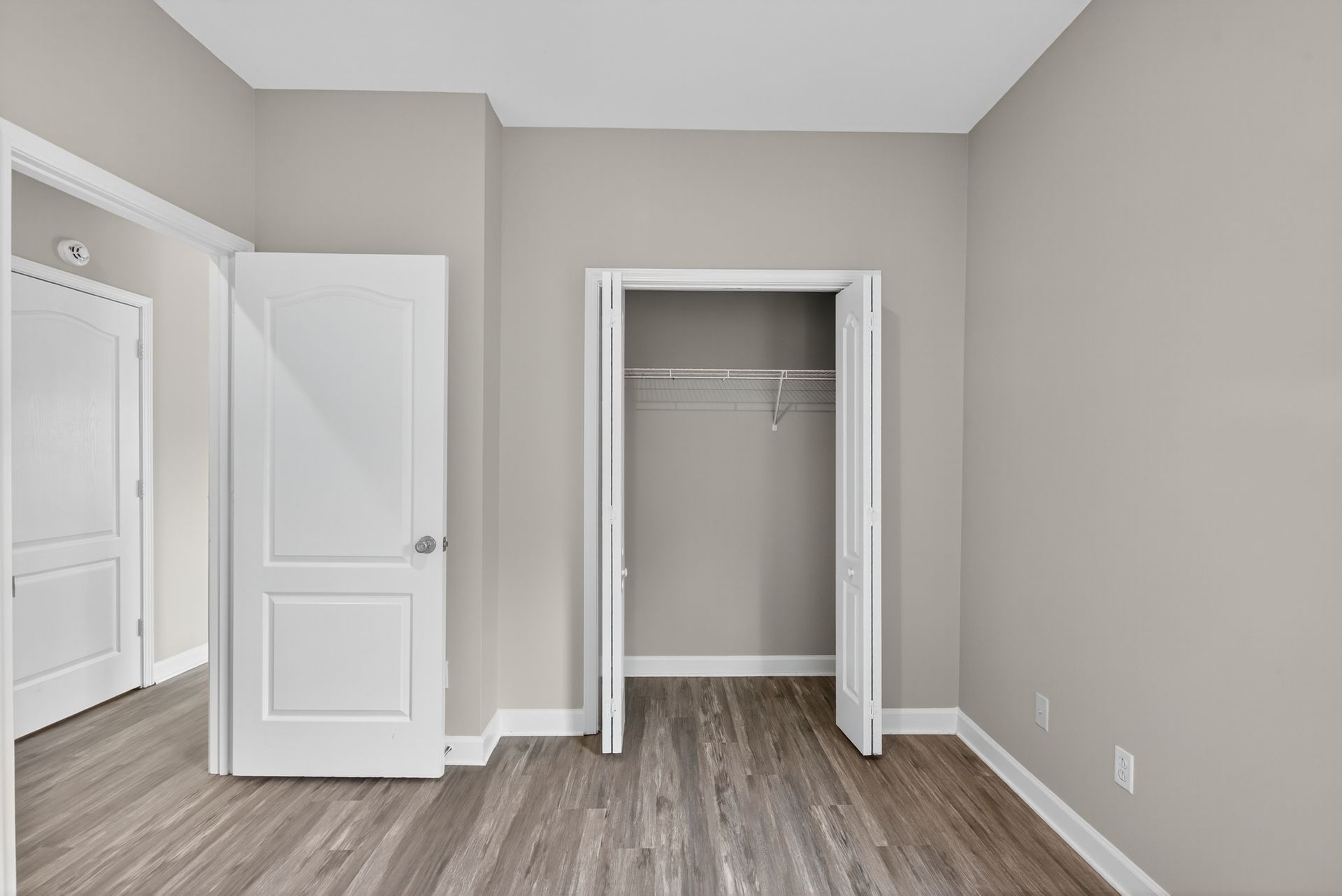 An empty room with light gray walls, wood-look flooring, a white interior door, and an open closet.