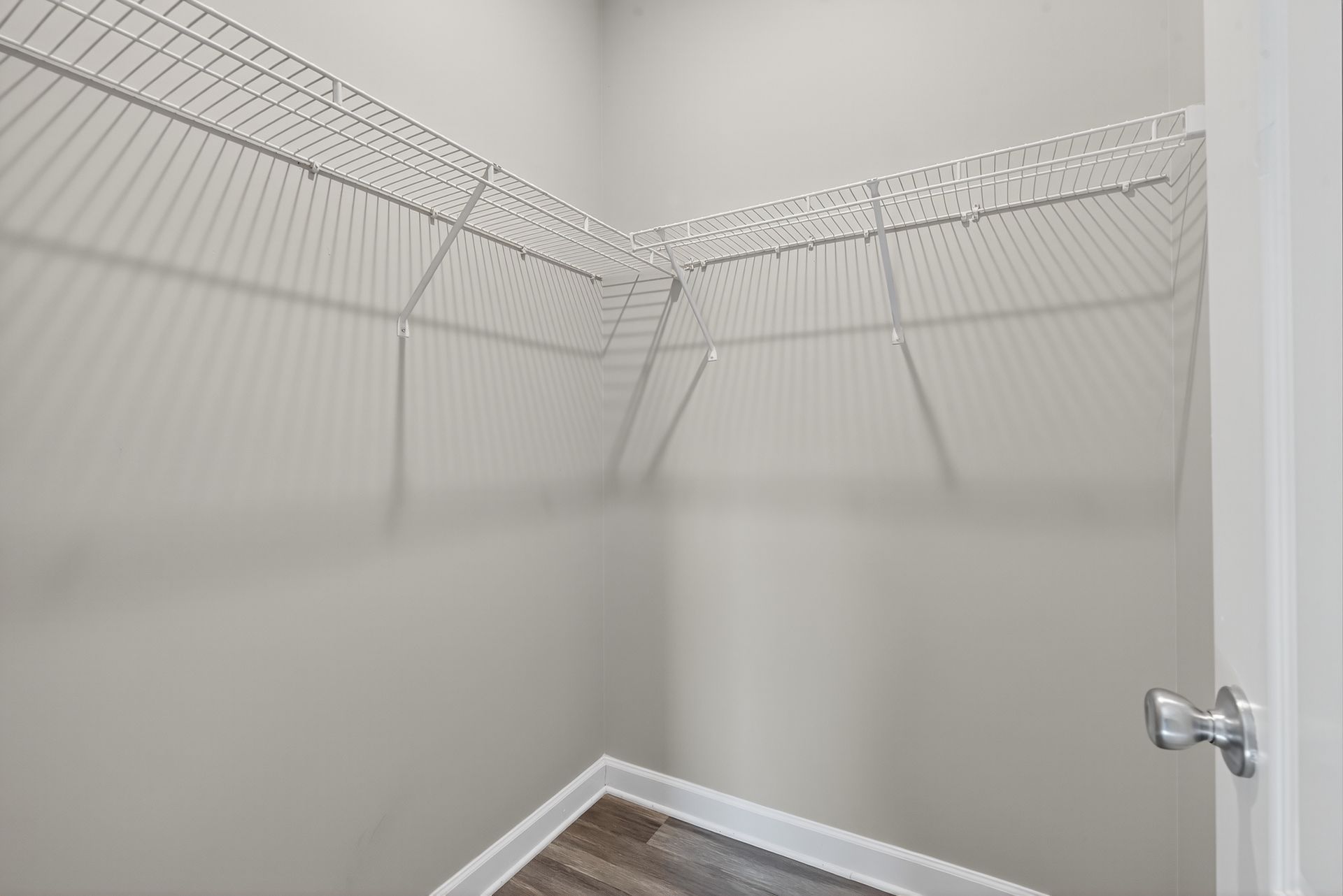 A small, empty closet with white wire shelving installed on two walls above a light grey floor.