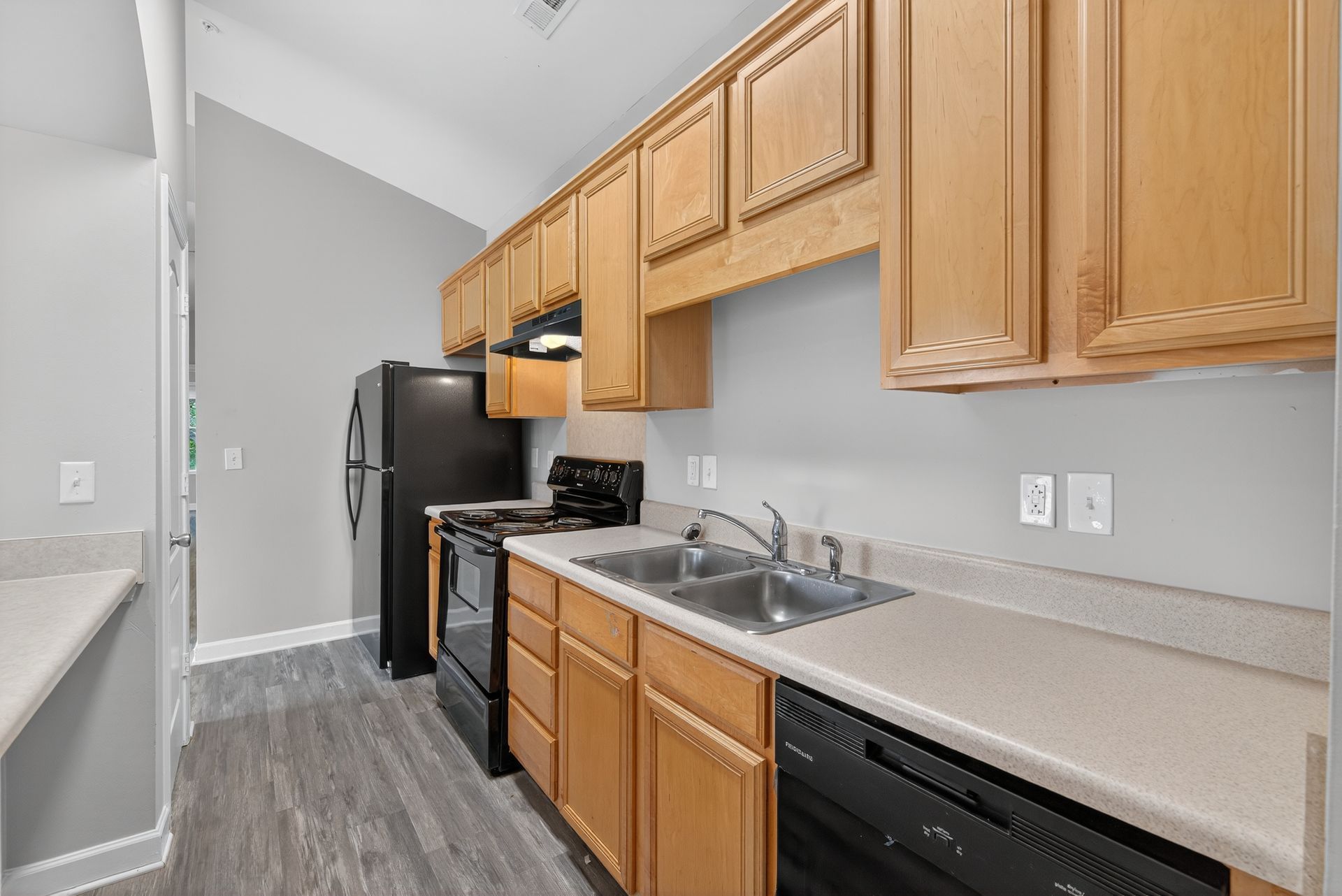 A kitchen with light-wood cabinets, gray walls, gray wood-look flooring, and black appliances.