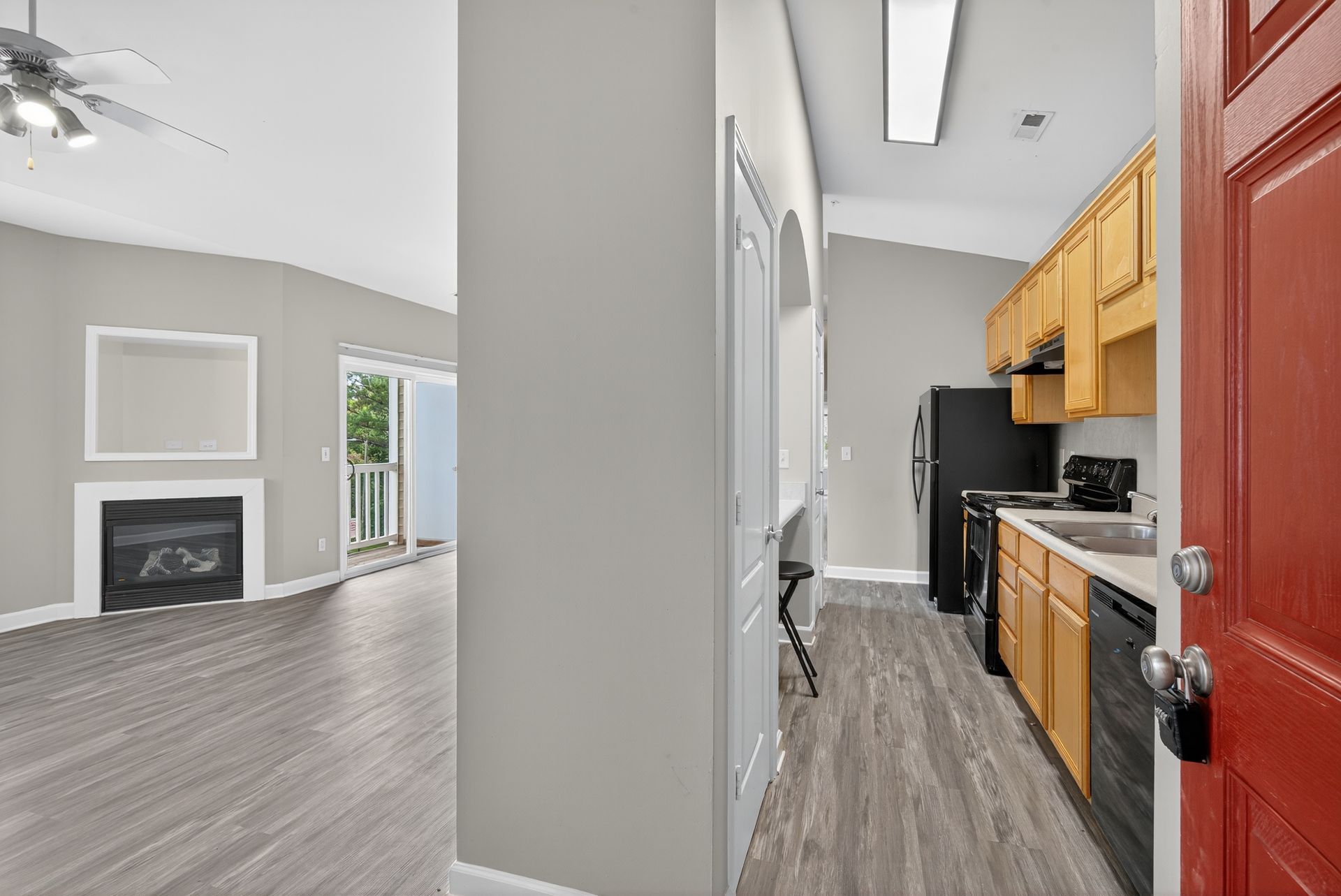 A view of a living room with a fireplace and a kitchen featuring wooden cabinets and light wood-look flooring.