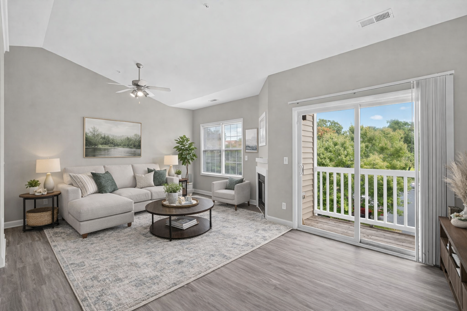 A modern, light-filled living room featuring a neutral sectional sofa, round coffee table, and a sliding door to a balcony.