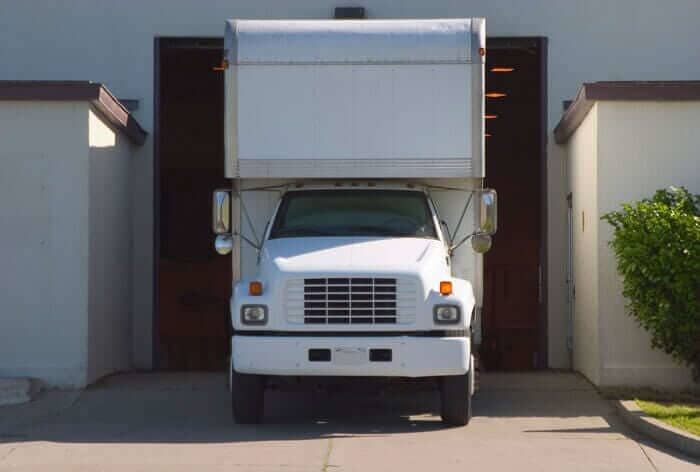 Un camión de mudanzas blanco está estacionado frente a la puerta de un garaje.