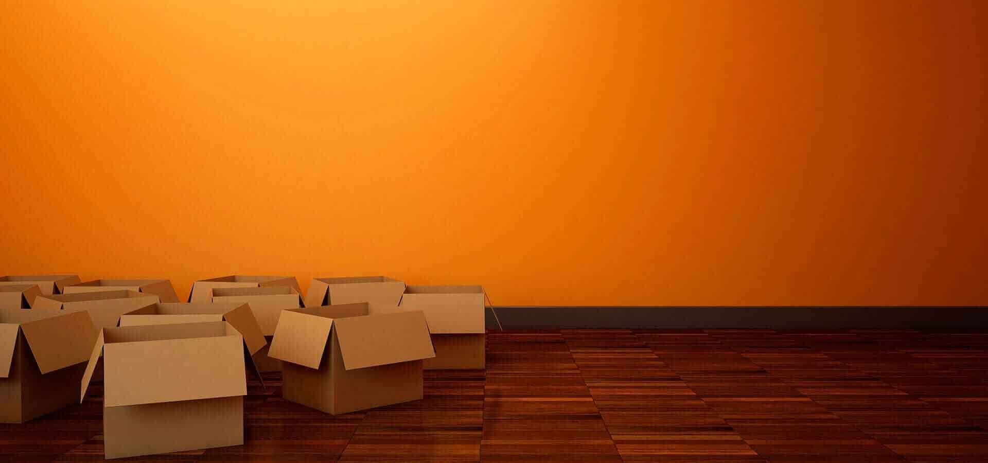 Una fila de cajas de cartón están colocadas sobre un suelo de madera frente a una pared naranja.