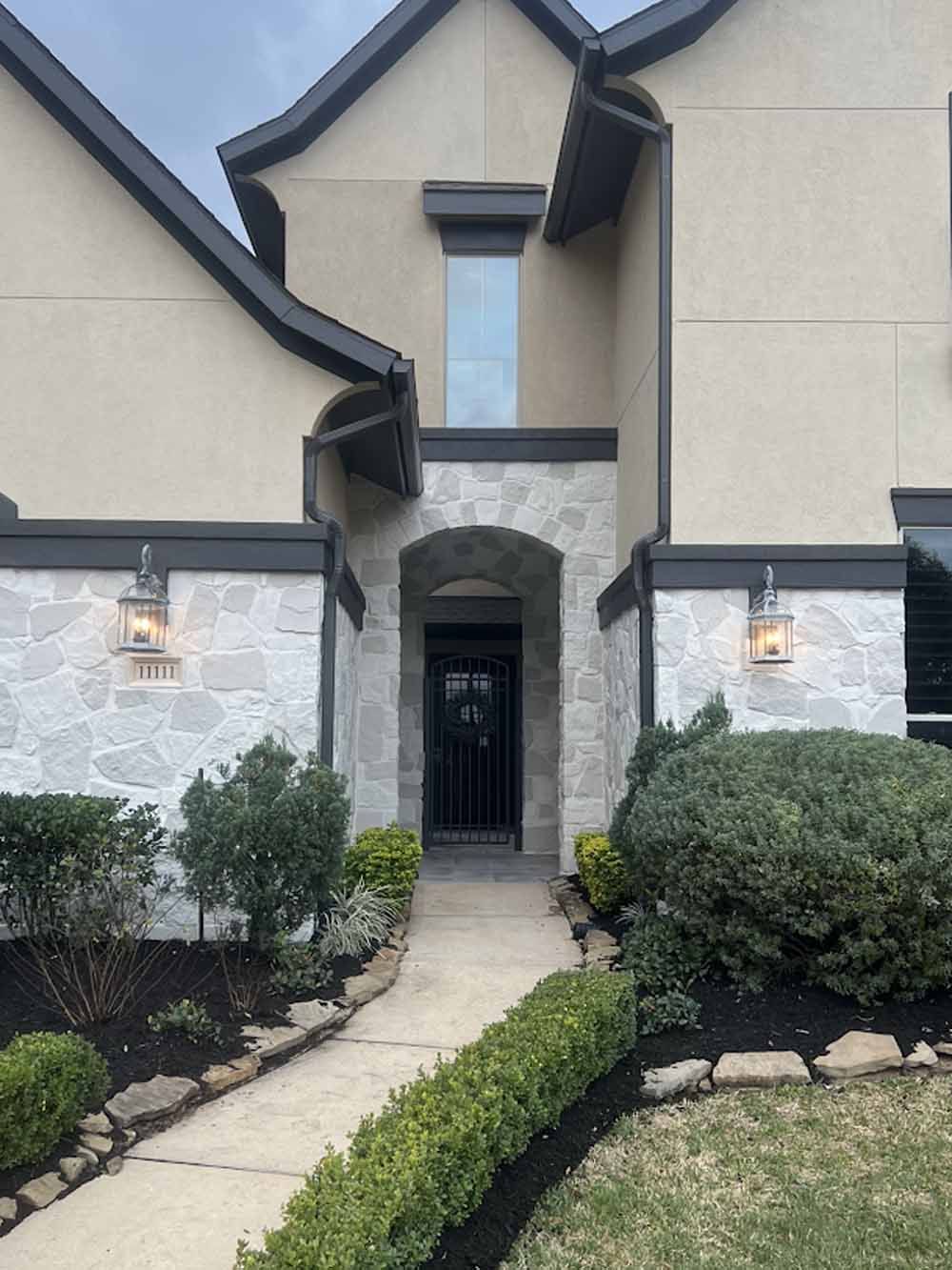 Beige house with stone entry, black trim, and path to door, landscaping.