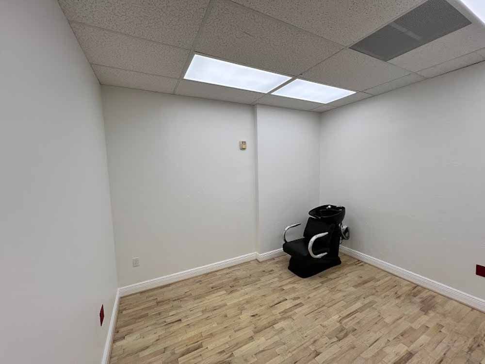 Empty white-walled room with wood-look flooring, a black chair, and ceiling lights.