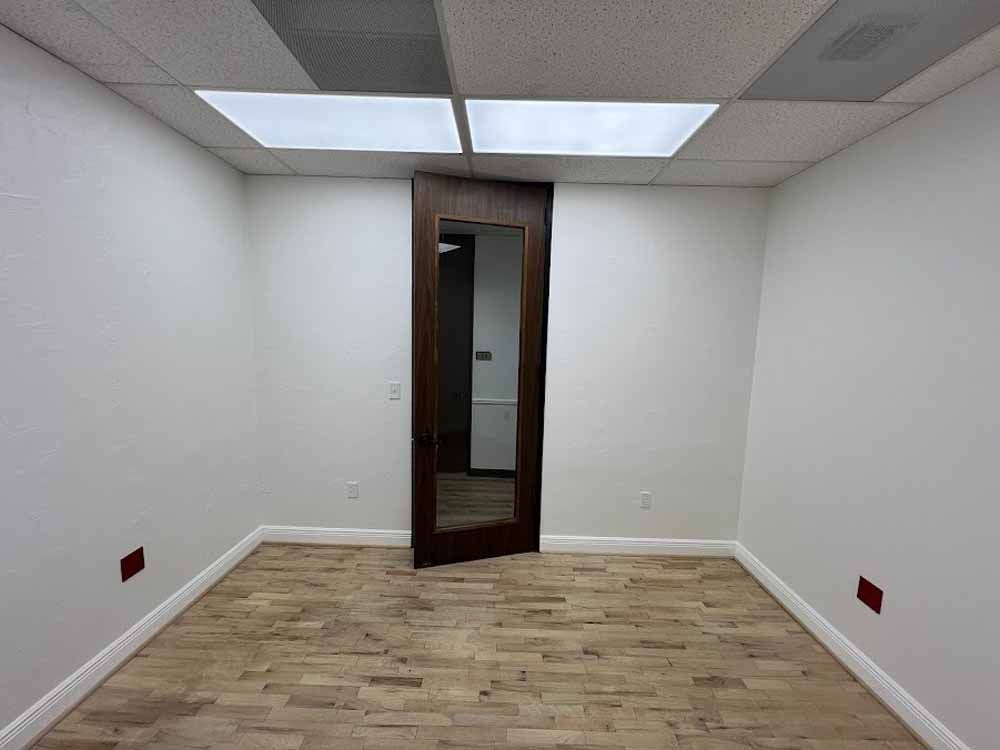 Empty office room with wood floor, white walls, and a dark wood door.