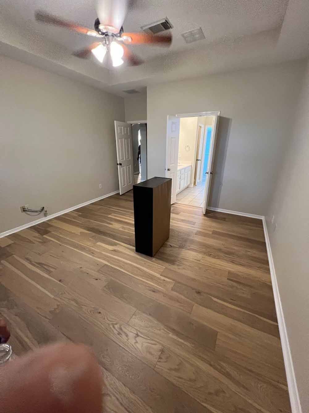 Empty bedroom with hardwood floors, doorway to bathroom, and a box in the center.