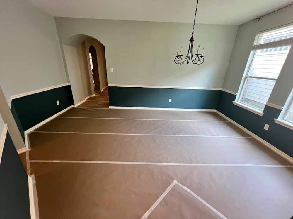 Dining room with two-toned walls (green and teal), chandelier, and floor covered with protective material.