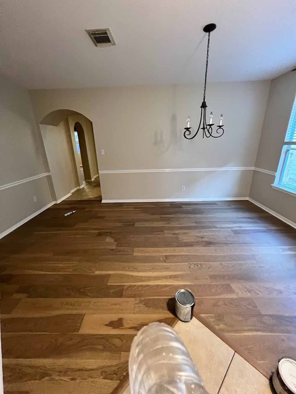 Newly installed hardwood floors in a room with cream-colored walls and a chandelier.