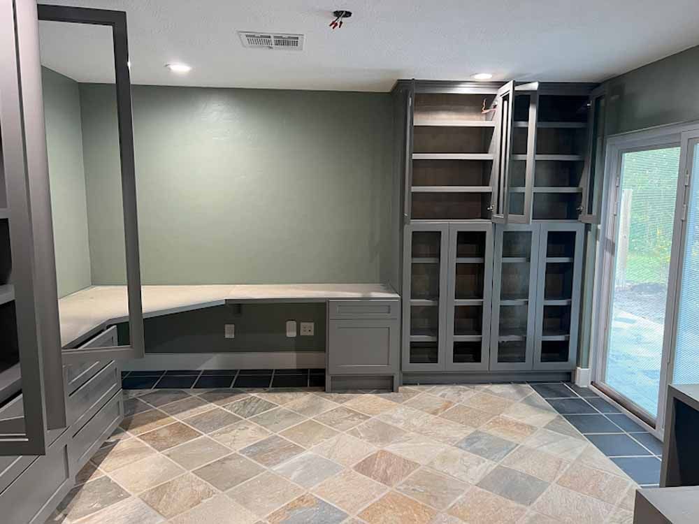 A home office with gray built-in cabinets, desk, and open shelves against a green wall, with a sliding glass door.