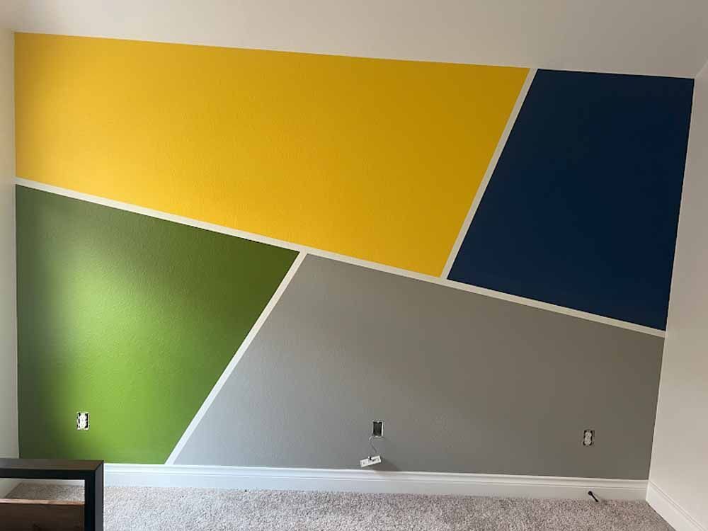 A wall painted with geometric shapes in yellow, green, navy, and gray.