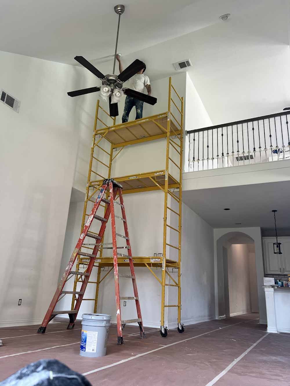 Person on a tall scaffolding working on a ceiling fan in a large room.