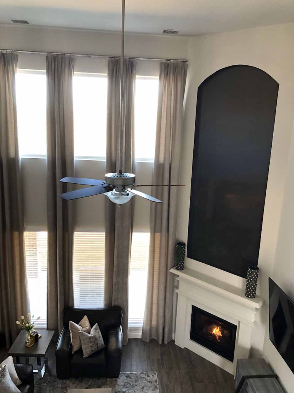 High-ceilinged living room with tall windows, fireplace, and a dark armchair.
