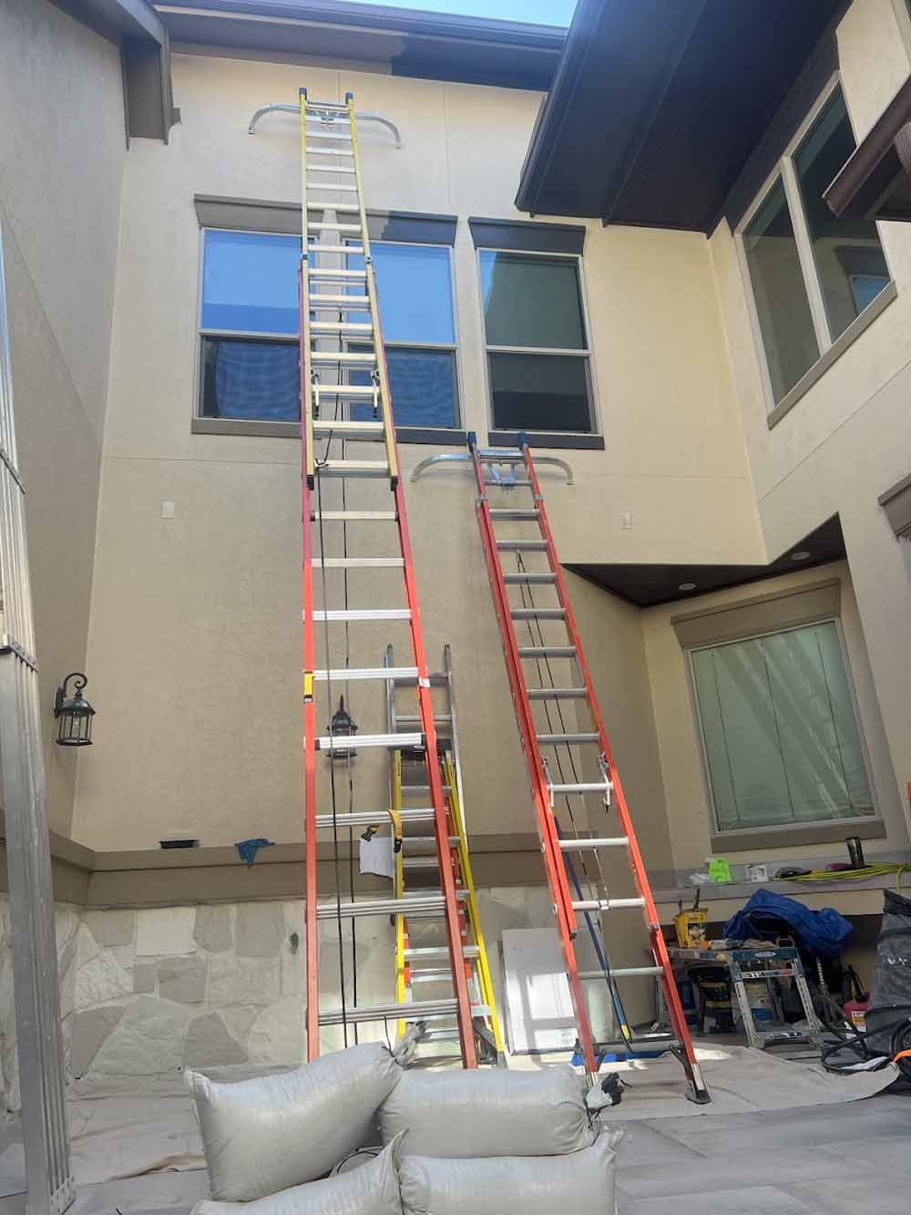 Three ladders against a beige building with windows. Construction supplies are nearby.