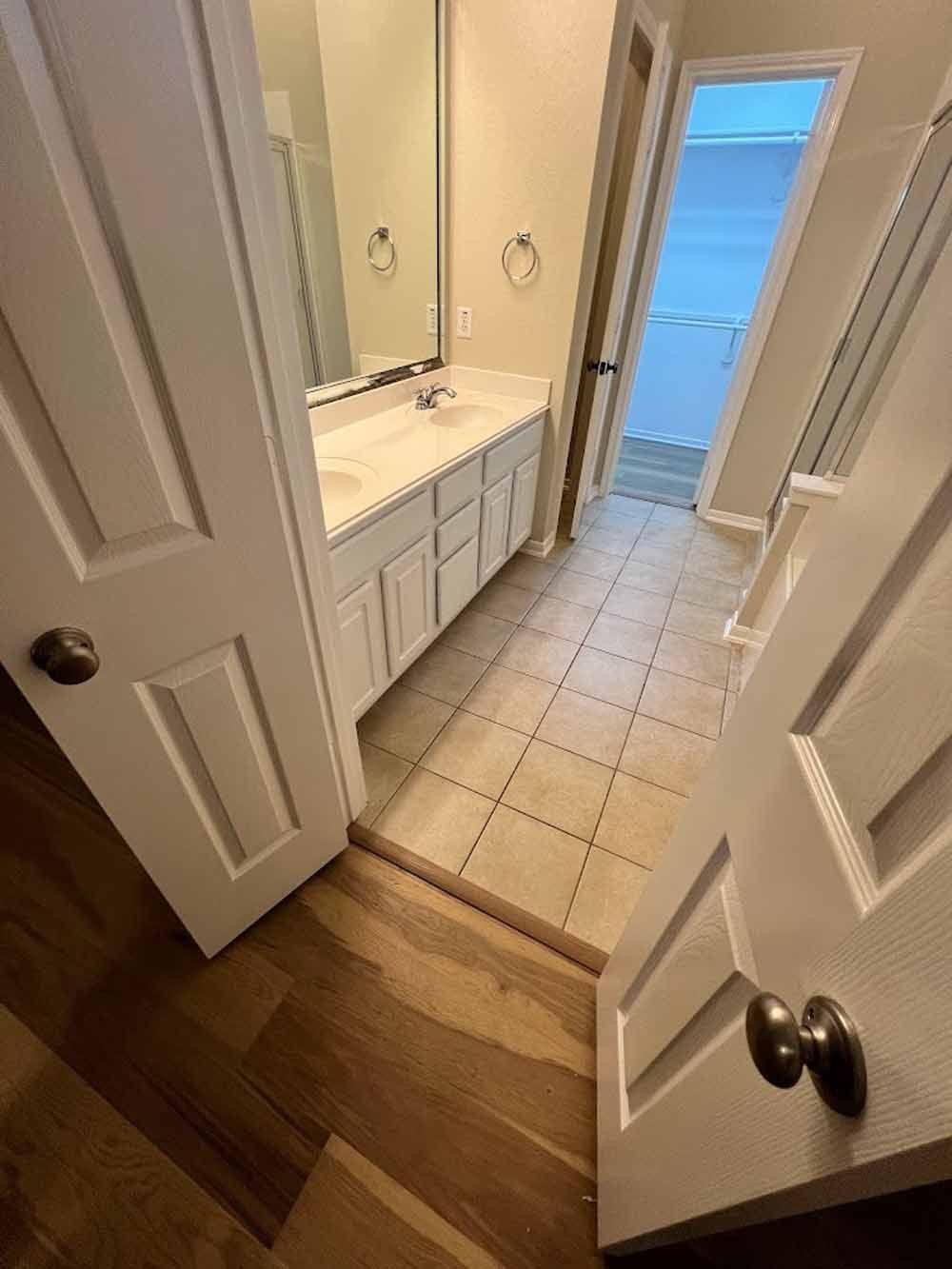 Bathroom entry with white cabinets, tile floor, and open doors.