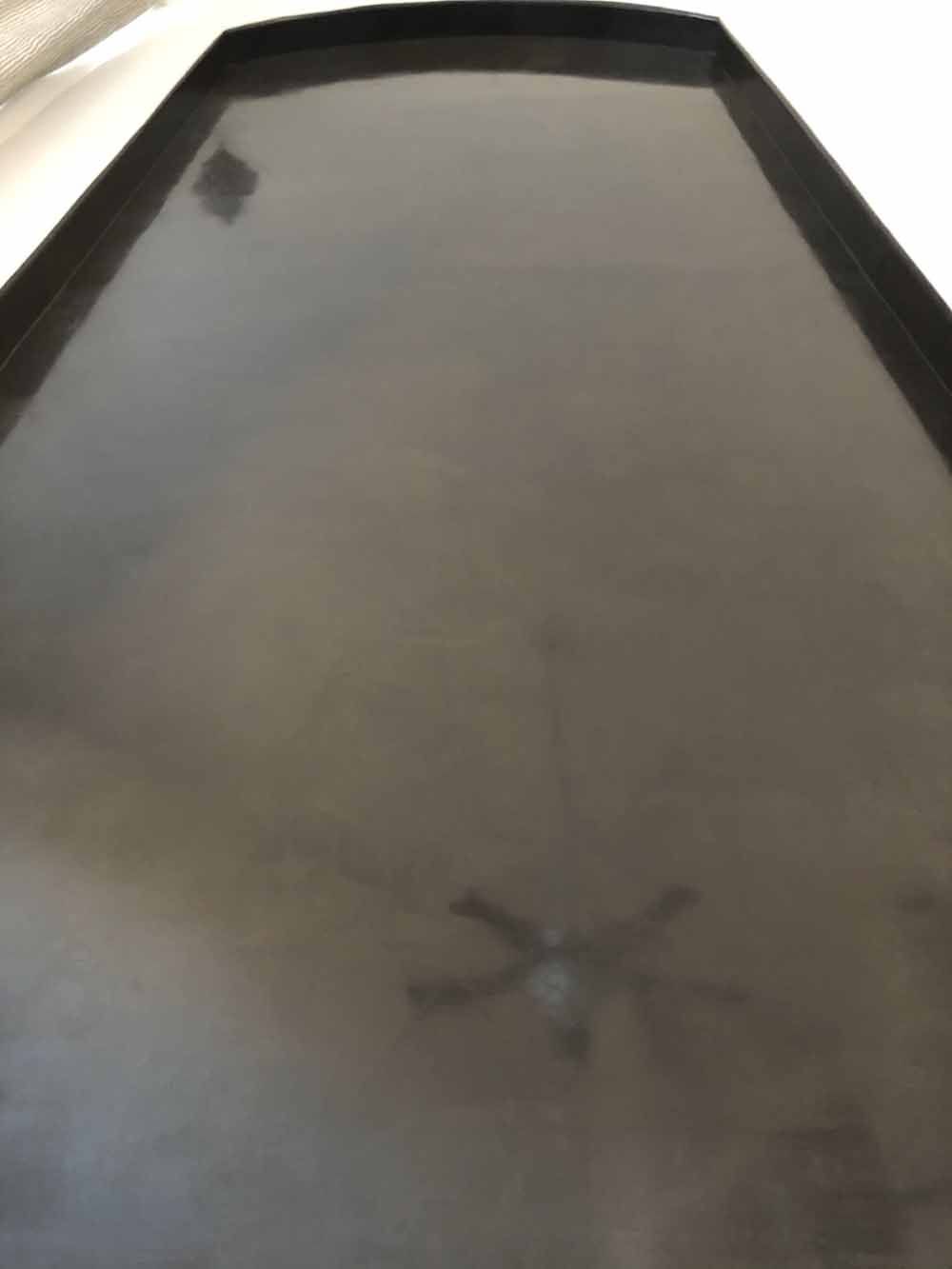 Reflective black surface, possibly a table or floor, with a ceiling fan reflected in the center.