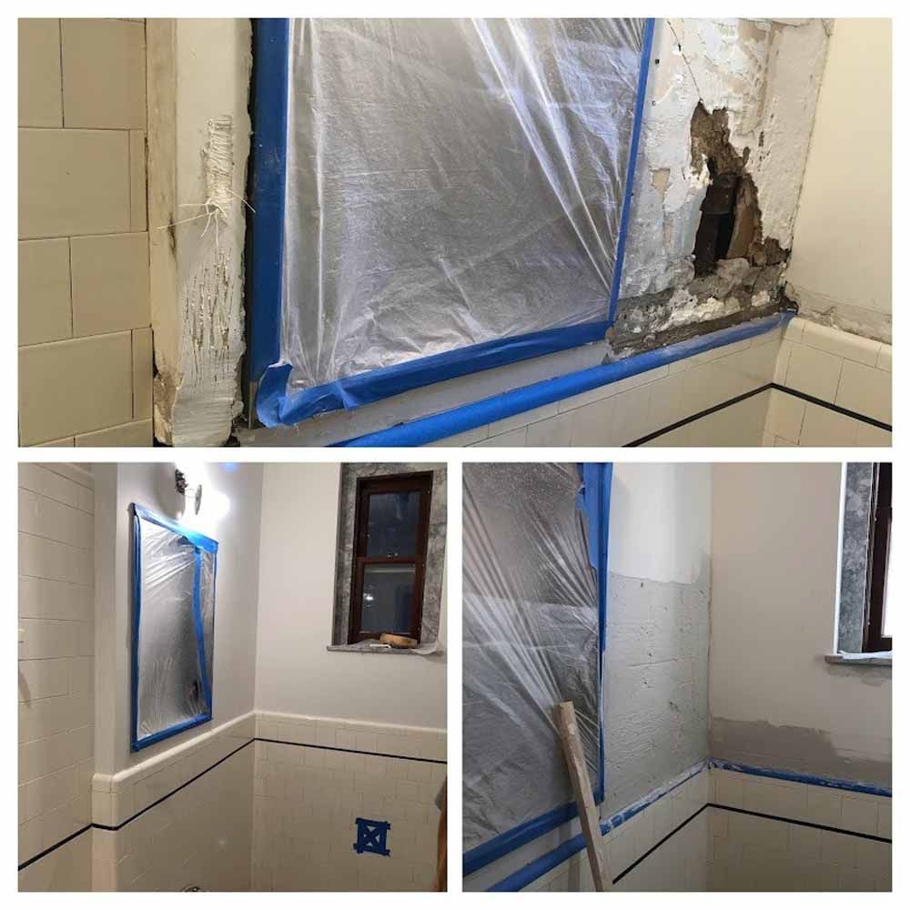 Bathroom wall repair in progress: blue tape, plastic covering, damaged plaster, and newly painted walls.
