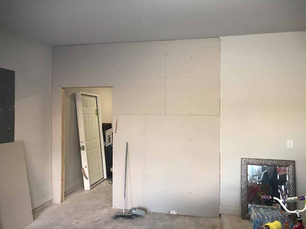 Room with a partially drywalled wall, doorway with door, and mirror against the wall.