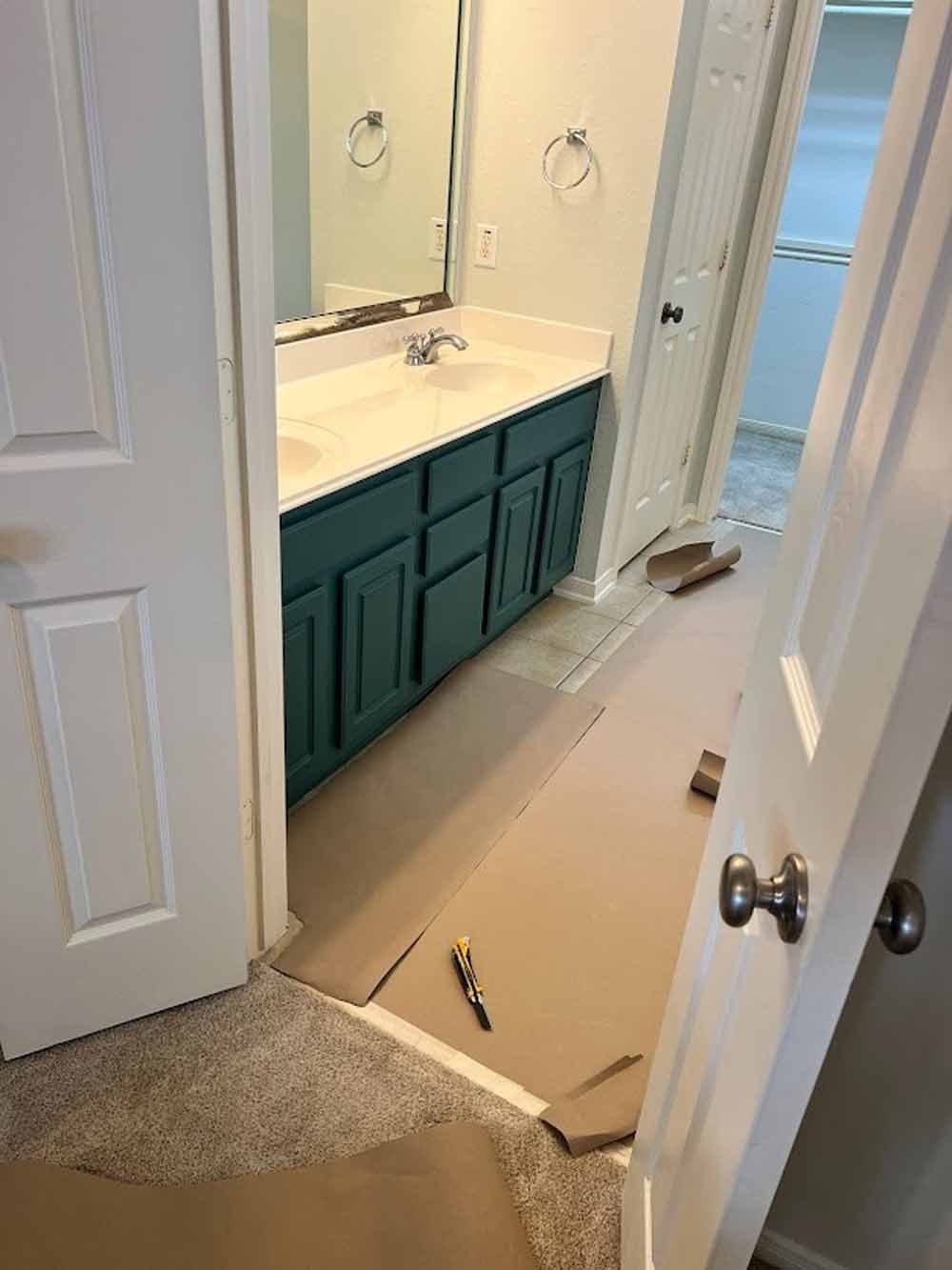 Bathroom renovation with blue vanity, cardboard protecting floor, open doors.